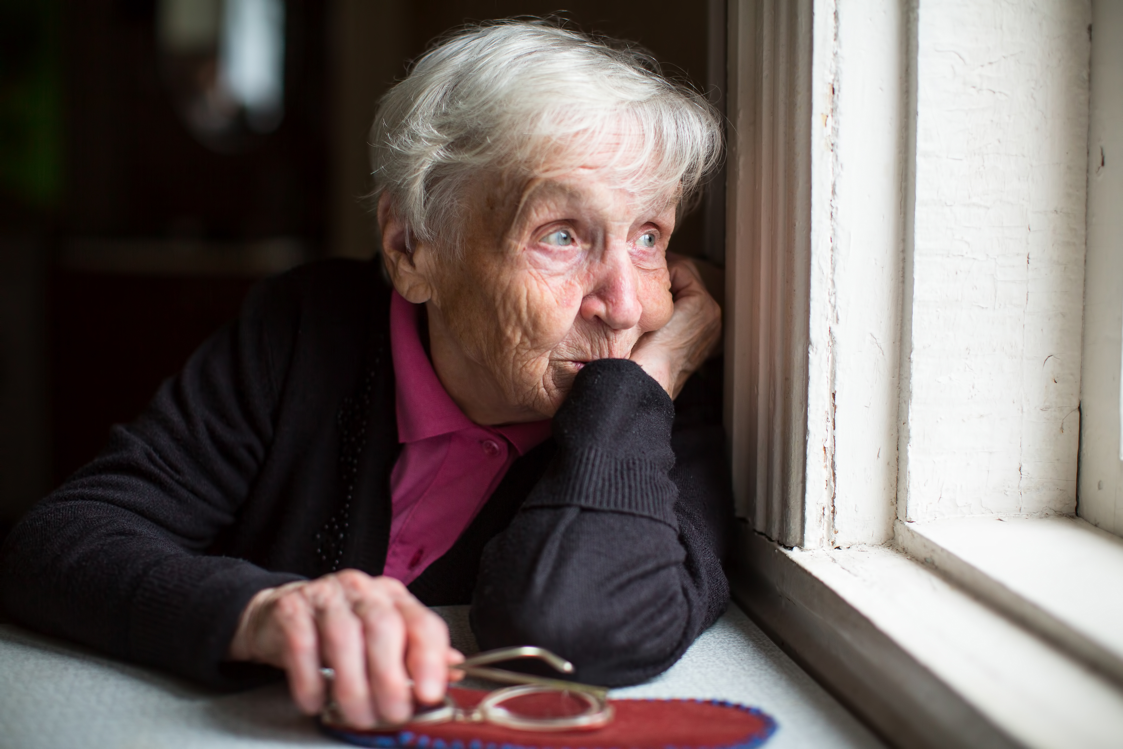 En äldre kvinna som tittar ut genom ett fönster